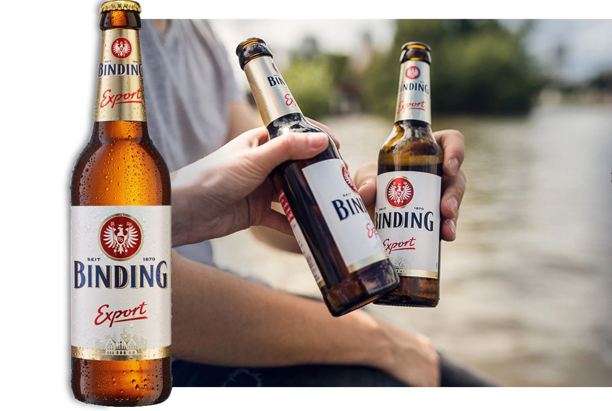 Zwei Hände halten Bierflaschen vor einem fließenden Fluss im Hintergrund.