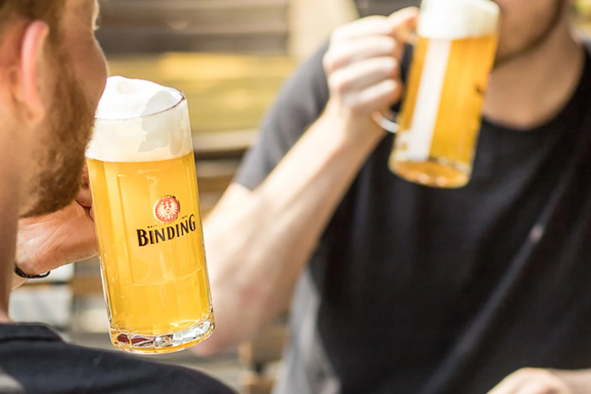 Zwei Personen stoßen mit Gläsern voll hellem Bier an.