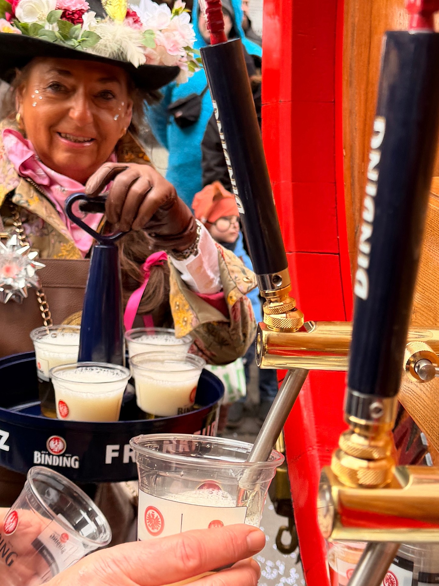 Mehrere verkleidete Personen zapfen sich Bier bei einem Binding-Zapfhahn ab.