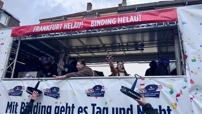Mehrere verkleidete Personen auf einem Binding-Fastnachtsumzugswagen werfen den Besuchern Süßigkeiten zu.