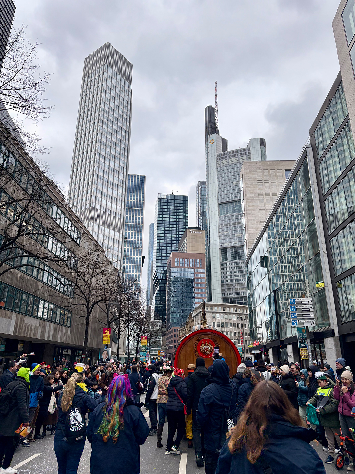 Zahlreiche verkleidete Personen nehmen an einem Fastnachtsumzug in Frankfurt teil. Im Hintergrund sind einige Hochhäuser.