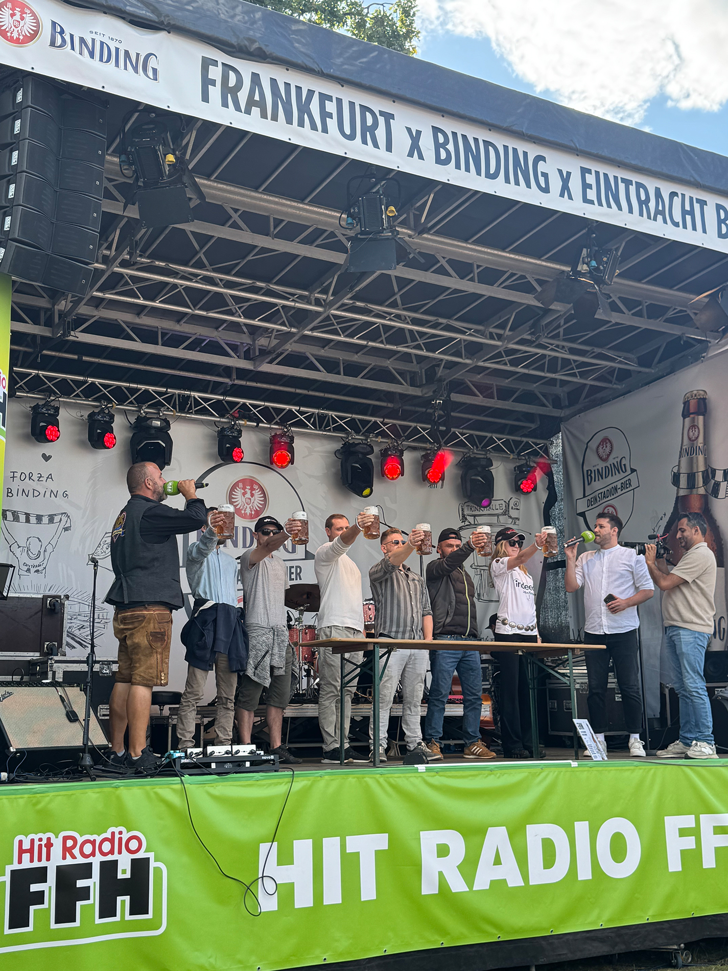 Eine Gruppe von Menschen macht einen Glas-Hochhalte-Wettbewerb auf der Binding und Radio FFH Bühne.