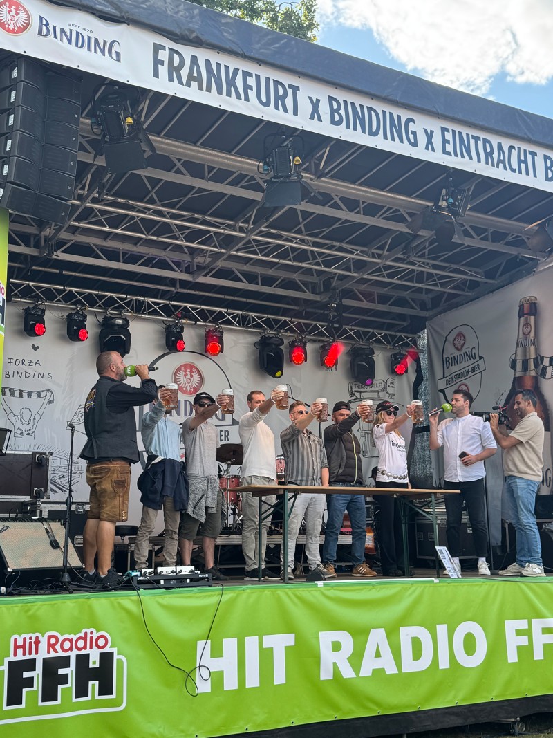 Eine Gruppe von Menschen macht einen Glas-Hochhalte-Wettbewerb auf der Binding und Radio FFH Bühne.