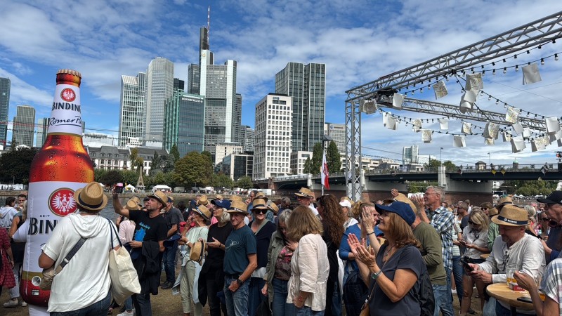 Viele Menschen laufen am Mainufer auf dem Museumsuferfest in Frankfurt, im Hintergrund die Frankfurter Skyline.