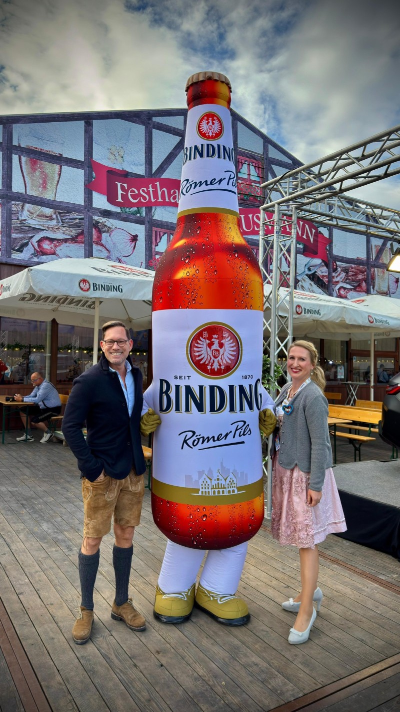 EIne übergroße Bindingflasche vor einem Bierzelt, rechts und links davon jeweils eine Person.