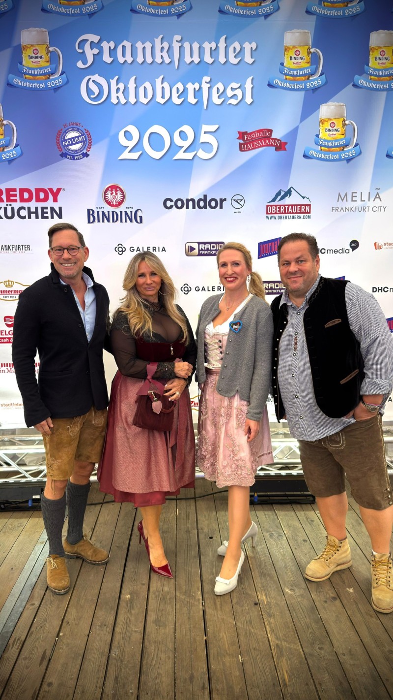 Vier Perosnen vor einem Banner auf dem Frankfurter Oktoberfest steht.