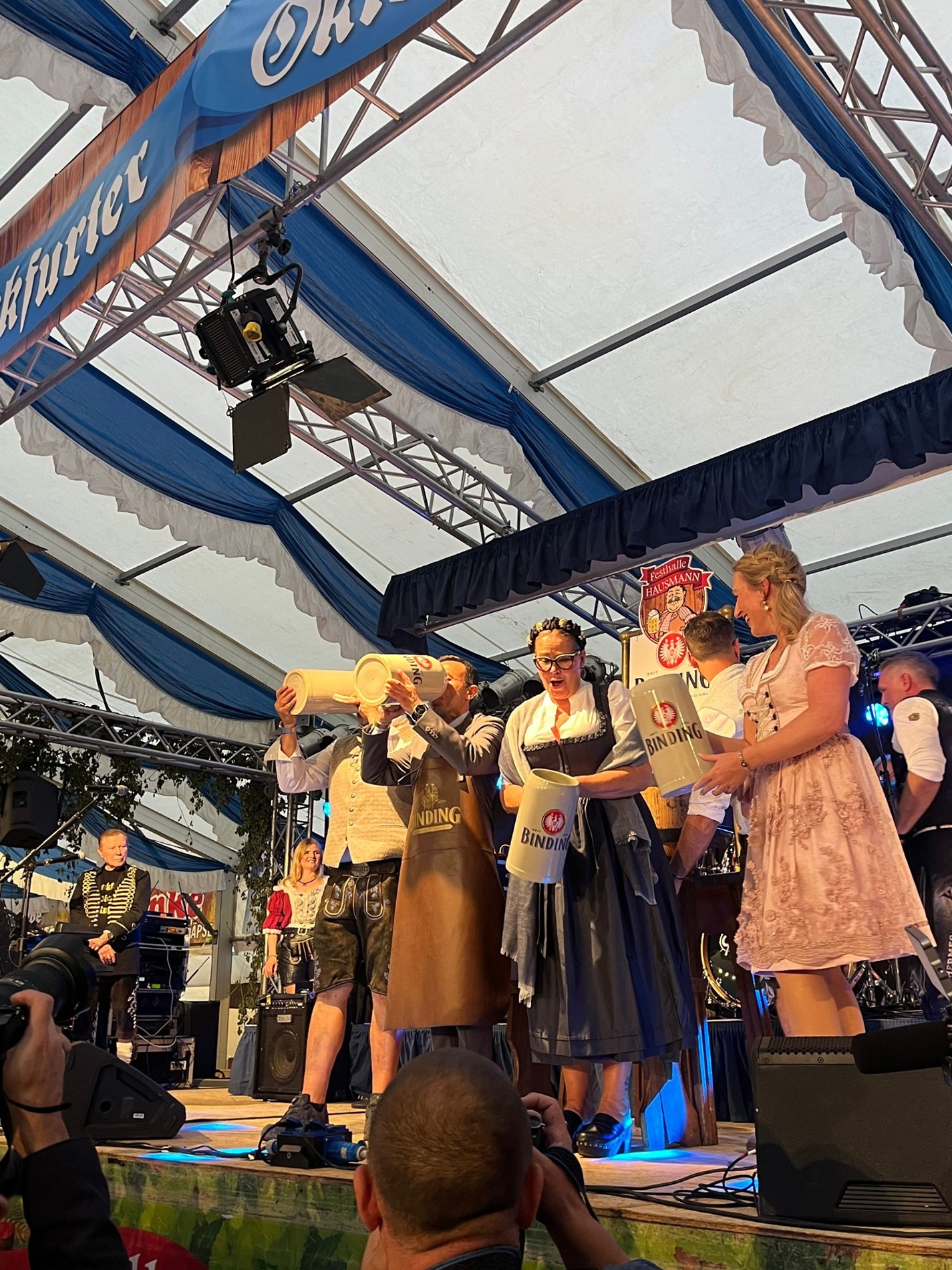 Vier Personen stehen mit Bierkrügen auf einer Bühne im Frankfurter Oktoberfest Festzelt.