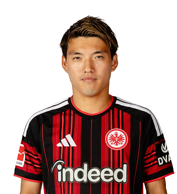 Mit seitlich gestylten dunklen Haaren und hellen Strähnen blickt der Mann im Eintracht Frankfurt Trikot frontal nach vorn.