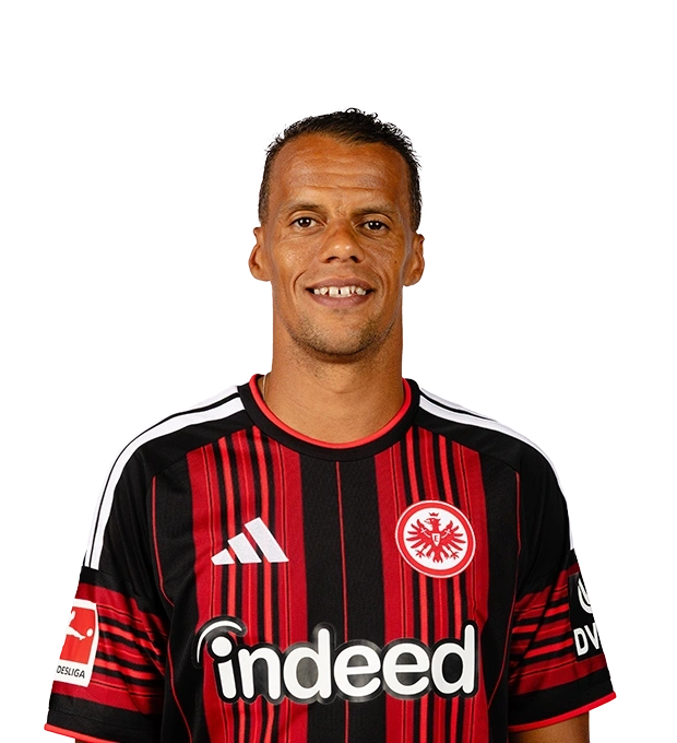 Ein lächelnder Mann mit kurzen dunklen Haaren und markanten Gesichtszügen trägt das Eintracht Frankfurt Trikot.