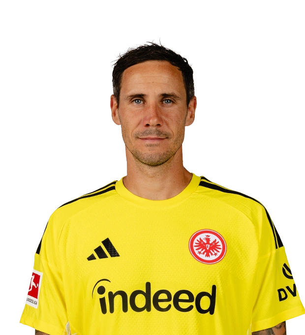 Ein Mann mit kurzen dunklen Haaren und leichtem Bart trägt ein leuchtend gelbes Eintracht Frankfurt Torwarttrikot.