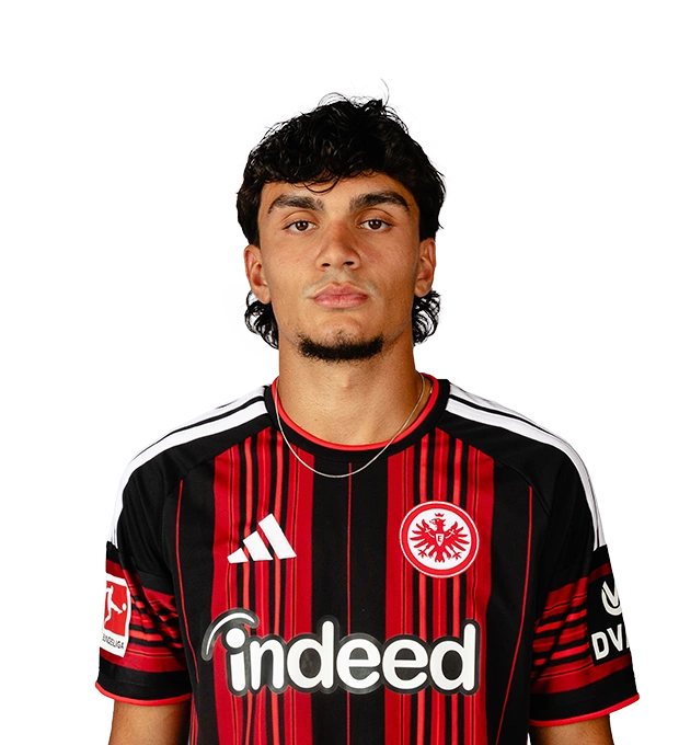 Lockige dunkle Haare, kurzer Kinnbart und eine feine Halskette trägt ein Mann im Eintracht Frankfurt Trikot.