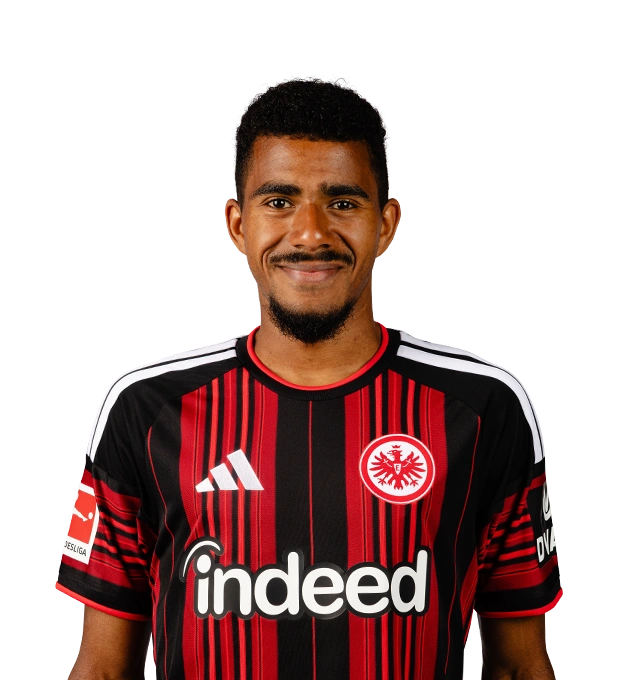 Lächelnder Mann mit kurzen schwarzen Haaren, Schnurrbart und Kinnbart trägt das Eintracht Frankfurt Trikot.
