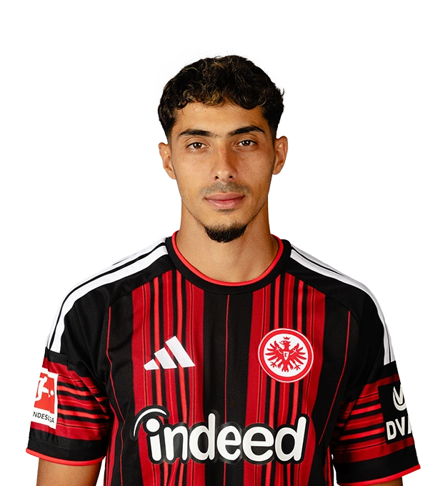Dunkle kurze Locken und ein schmaler Kinnbart umrahmen das Gesicht eines Mannes im Eintracht Frankfurt Trikot.