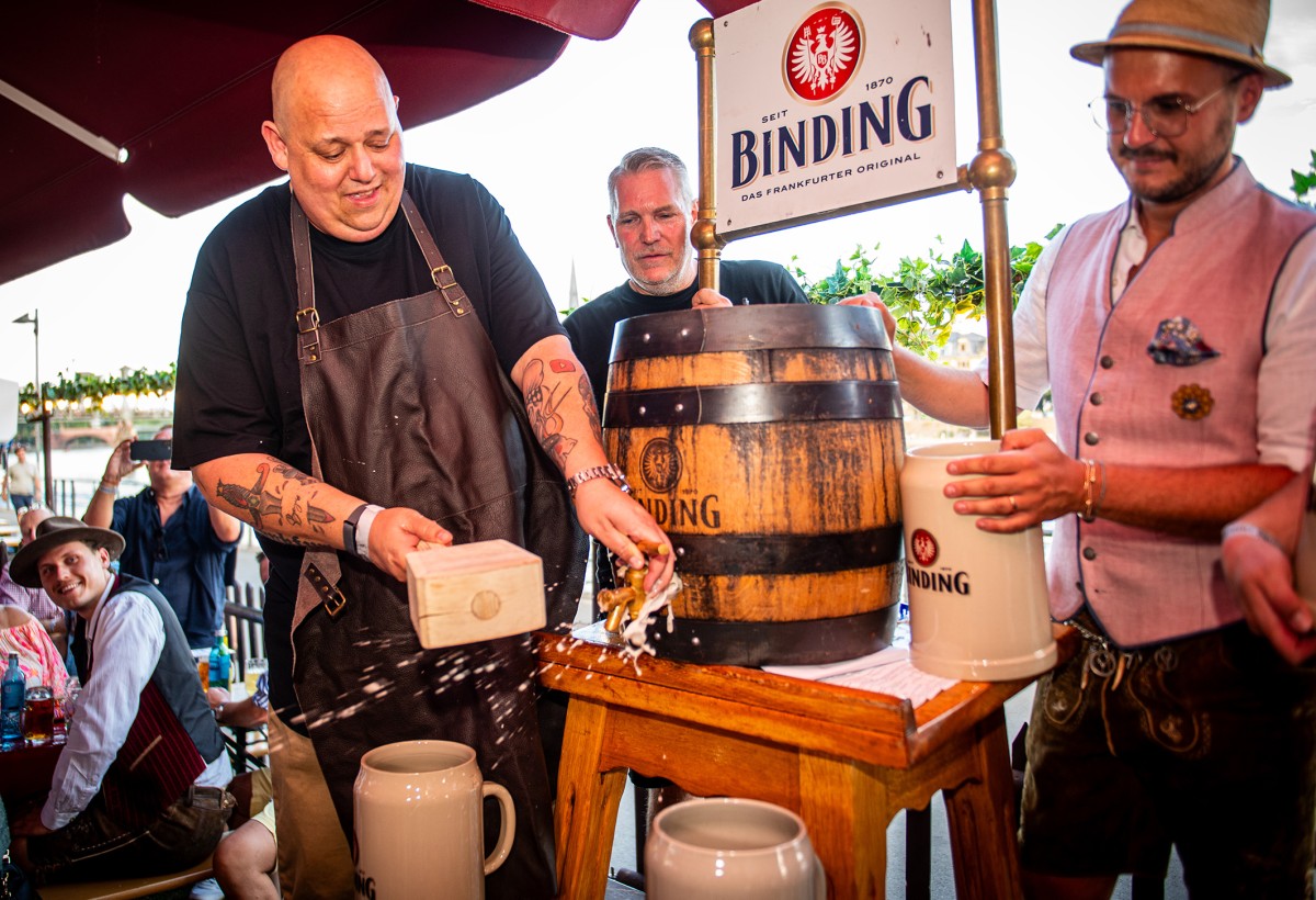Eine Personen sticht ein Binding Festbier Bierfass an, daneben weitere Personenen mit Bierktügen.